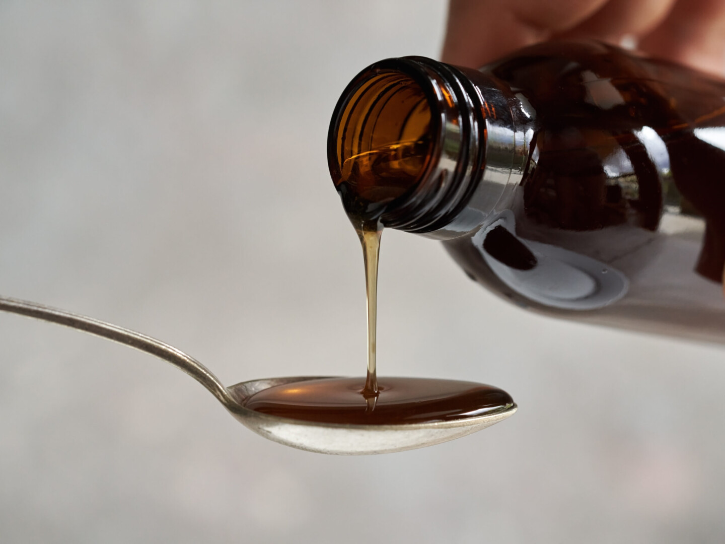 Herbal syrup being poured from a dark bottle onto a metal spoon