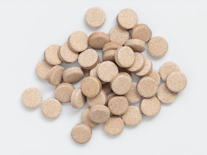 Close-up of a stack of beige herbal capsules on a gray background.